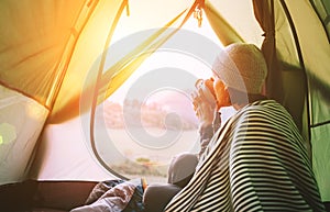 Morning in temt camp.Woman with cup of hot tea sit in camping tent