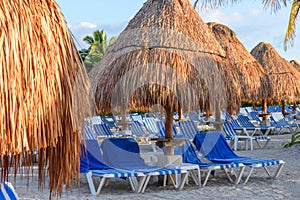 Morning tropical sandy beach with straw umbrellas and lounge chairs.