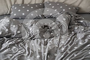 morning unmade messy bed with gray blanket and pillows