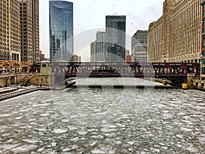 Morning view of frozen Chicago River and surrounding cityscape during heavy snowfall.