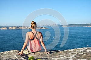 Morning view of a young female hiker sitting on a rock at North Head, a headland in Manly.