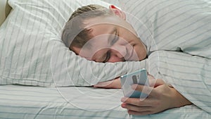 In the morning after waking up, a man lies in bed and looks at the news in his phone, camera tracking