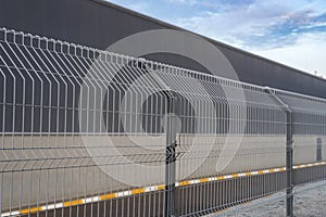 Morning winter frost on the steel grating fence made with wire on blue sky background. Sectional fencing installation.