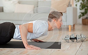 Morning workout. Handsome guy doing push-ups on mat in living room photo