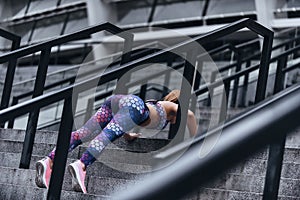 Morning workout. Modern young woman in sport clothing keeping plank position while exercising on the steps outdoors