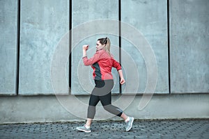 Morning workout. Side view of young plus size woman in sport clothes running outdoors.