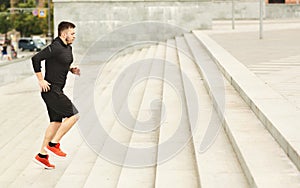 Morning workout. Young Athlete running up on stairs against cityscape