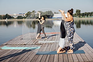 Morning yoga class on a wooden pier in the city. Young women stand in a headstand on mats. The instructor helps to do the exercise