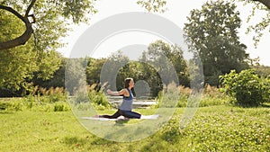 Morning yoga in park. Meditation concept. Young serene woman meditating in summer park at sunrise. Female sitting on fitness mat,