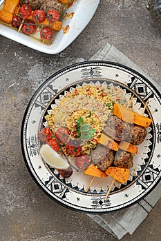 Moroccan couscous with lamb kebab on skewers on traditional plate