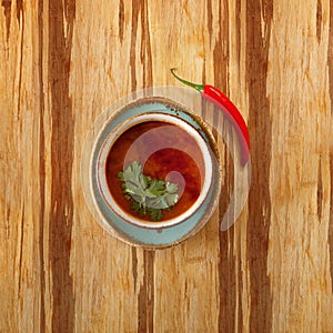 Moroccan food, tomatoe soup dish decorated with parsley, on a plate with red hot chili pepper, on a wooden table