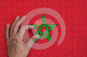 Morocco flag is depicted on a puzzle, which the man`s hand completes to fold