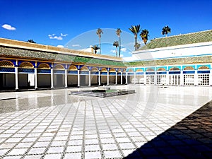 Morocco. Palace El Bahia Marakesh. Interior courtyard with white floor and row of columns on a background of palm trees and blue s