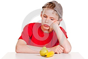 Morose young boy staring at a ripe banana and pear