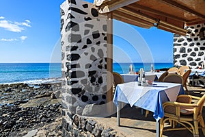 MORRO JABLE, FUERTEVENTURA - FEB 7, 2014: tables and chairs of a restaurant on coast of Morro Jable town. Building is made of lava