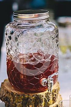 Morse or berry juice in glass jar beverage dispenser stands on a wooden slice