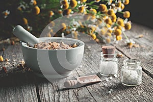 Mortar of dried healing herbs, homeopathic globules and bunch of chamomile plant.