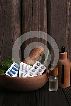 Mortar with fresh green herbs, extracts and pills on wooden table