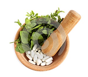 Mortar with fresh green herbs and pills on white background, top view