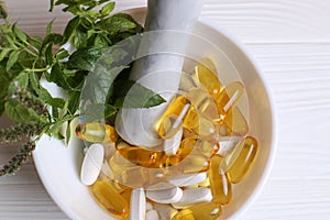 Mortar with fresh green herbs and pills on white wooden table, top view