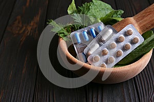 Mortar with fresh green herbs and pills on wooden table, closeup. Space for text