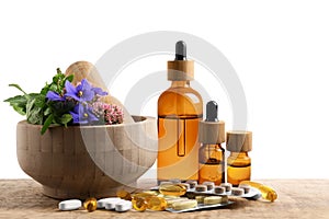 Mortar with fresh herbs, extracts and pills on white background
