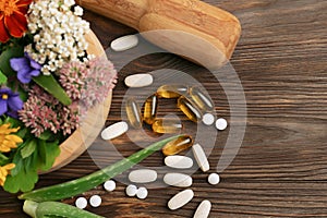 Mortar with fresh herbs, flowers and pills on wooden table, flat lay
