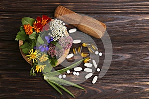 Mortar with fresh herbs, flowers and pills on wooden table, flat lay