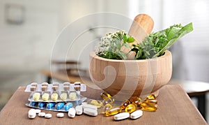 Mortar, fresh herbs and pills on wooden surface in medical office