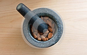 A mortar full of almonds with a pestle on top