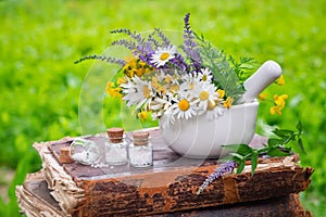 Mortar of healing herbs, bottles of homeopathic globules and old book outdoors.