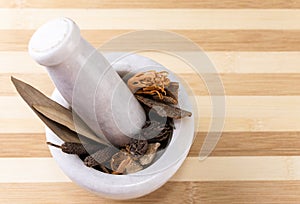 Mortar and pestle close-up shot with pepper, aril, black cardamom, dry ginger and cinnamon sticks on a striped wooden background. photo