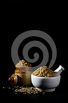 Mortar and pestle with Coriander Powder and seeds on black background