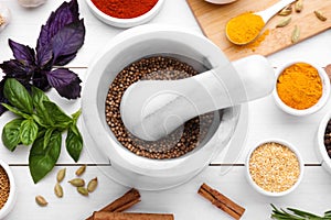 Mortar with pestle and different spices on white wooden table, flat lay