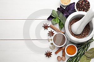 Mortar with pestle and different spices on white wooden table, flat lay. Space for text