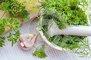 Mortar and pestle with fresh green herbs spices. Fresh dill, parsley, arugula and garlic on wooden board and white towel