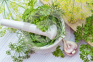 Mortar and pestle with fresh green herbs spices. Fresh dill, parsley, arugula and garlic on wooden board and white towel