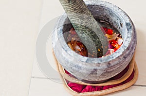 A mortar and pestle or lesung batu in Malay with crushed chilies, fried shallots and shrimp paste mixed together.