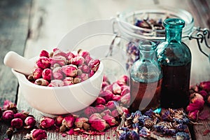 Mortar with rose buds, bottles of tincture and dried flowers photo