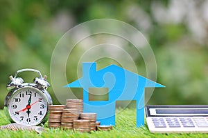 Mortgage calculator, Blue house model and stack of coins money with alarm clock on natural green background,Interest rates and