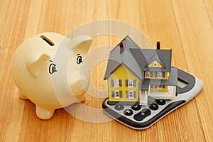 Mortgage calculator with a house and piggy bank on a wood desk
