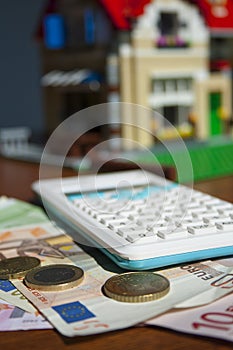 Mortgage concept with blurred background focused on bills, coins and calculator, house concept on background. Vertical format