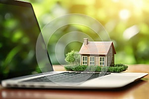 Mortgage concept with a house model on a laptop keyboard against a green nature background. Real estate, finance, and eco-