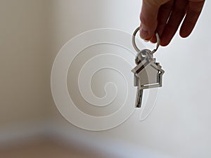 Mortgage concept. Women hand holding key with house shaped keychain. Modern light lobby interior. moving home or