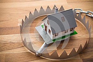 Mortgage house in a trap on wooden table background. House trap on debt or loan problem or risk in real estate property financing