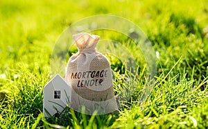 Mortgage lender money bag and house in a grass.