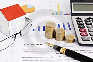 Mortgage loans concept with close up business fountain pen and money coins stack and calculator and paper house and eyeglasses on photo