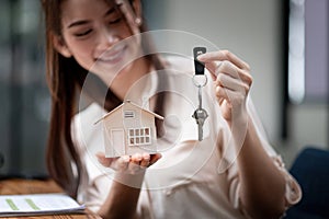 mortgage, real estate and property concept - close up of hands holding house model and home keys at modern office