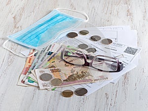 Mortgage and utility bills, coins and rubles banknotes, glasses and medical mask on wooden table.