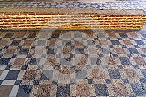 Mosaic floor of square geometric figures in blue and red colors and the remains of a Roman brick wall from the archaeological